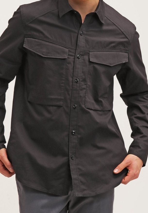 Camicia nera con bottoni realizzata in tessuto liscio, dotata di due tasche sul petto, colletto e orlo dritto con una vestibilità leggermente ampia.