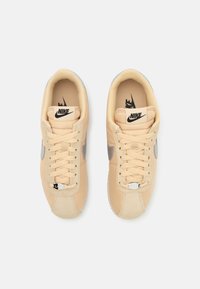 Rudi Nike sportbačiai su lygiu oda, pilku akcentu swoosh ir balta padanga. Sukurti su klasikiniais raišteliais ir perforuota nosies dizainu.