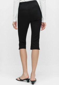 Svarta capri leggings tillverkade av stretchigt tyg, med hög midja och rullade muddar. Bakfickor är synliga, med en slät yta.