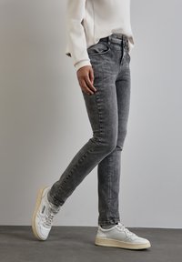 Jeans gris à coupe slim, présentant une texture délavée et un design classique à cinq poches, associés à des baskets blanches.