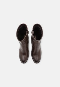 Bottes courtes en cuir marron au design élégant, bout rond et fermeture éclair latérale. Texture lisse avec des détails de couture minimalistes.