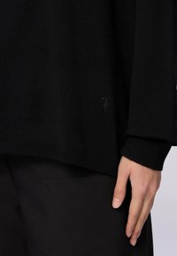 Czarny sweter z dzianiny z szerokimi rękawami i prążkowanymi wykończeniami. Dyskretne detale z logo w pobliżu dołu. Gładka tekstura, luźny krój.