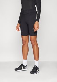 Sorte sykkelshorts med glatt tekstur og elastisk midjebånd, brukt sammen med en tettsittende langermet topp og svarte treningssko.