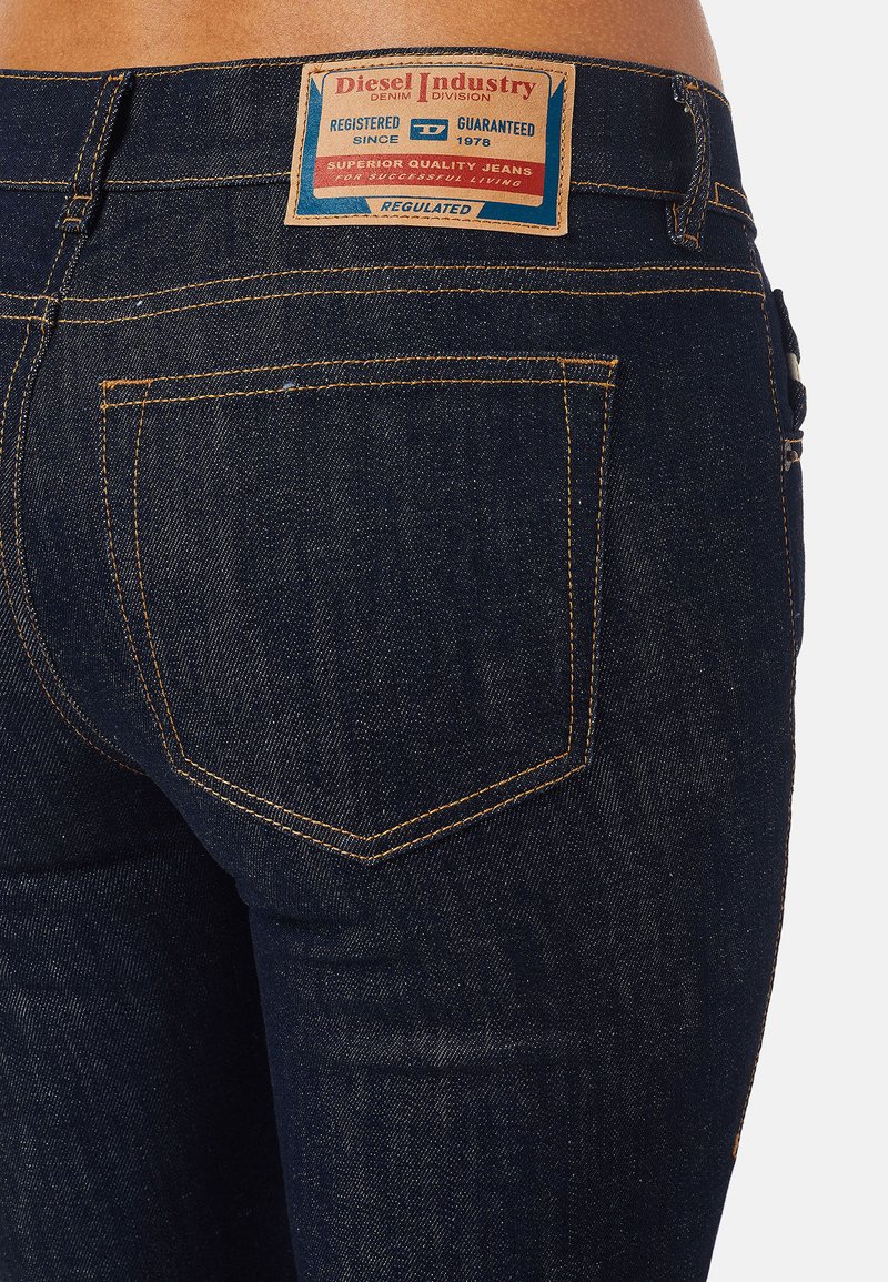 Jeans de mezclilla azul oscuro con un clásico diseño de cinco bolsillos, costuras amarillas y un parche de cuero con la marca en la cinturilla trasera.