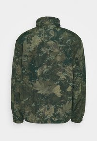 Bundy s maskáčovým vzorem v zelených odstínech, s stojatým límcem a elastickými manžetami. Materiál vypadá lehký a hladký na dotek.