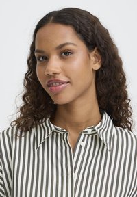 Randig skjorta i off-white och mörkgrön tyg, med knäppning fram och krage, med synlig textur och subtil lyster.
