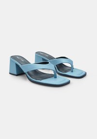 Light blue heeled sandals with a flat toe strap and square heel. Smooth texture with black interior and stitching details.
