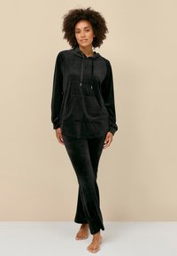 Zwart velours loungepak met een capuchonpullover met een voorzak en bijpassende uitlopende broek. Zachte textuur en een ontspannen pasvorm.