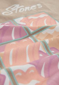 Gros plan sur un tissu avec des formes abstraites rose pastel, violet et beige, entourées de bleu sarcelle, et texte blanc partiellement visible "Stones".