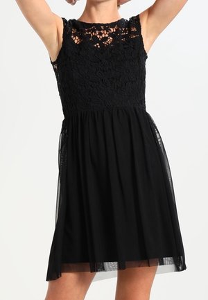 Sort kjole med blomsterbroderi på overdel, ærmeløs design og en svajende nederdel lavet af gennemsigtigt materiale. A-linje silhuet med en struktureret overdel.