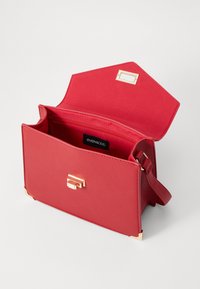 Crvena kožna torba s strukturalnim dizajnom, zlatnim detaljima i preklopom. Unutrašnjost sadrži zip džep i oznaku s logotipom.