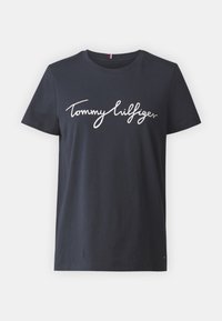 Camiseta de algodón azul marino con mangas cortas y cuello de tripulación, que presenta el logo en cursiva "Tommy Hilfiger" en blanco en la parte delantera.