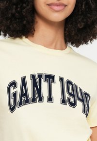 Sárga pamut póló tengerészkék "GANT 1940" ívelt felirattal, kerek nyakkivágással és rövid ujjakkal. Puha tapintású anyag.