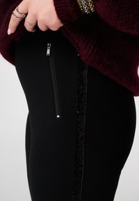 Zwarte legging met een zijrits en een verticale paillettendetail. De stof lijkt zacht met een gladde textuur. De tailleband zit hoog.