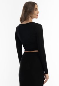 Sort, langærmet, cropped top med en tætsiddende pasform. Stoffet ser glat og blankt ud, kompletteret af en matchende høj talje nederdel.