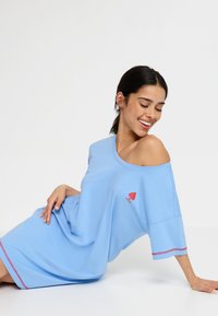 Gaiši zils lielgabarīta kleita no mīksta auduma, ar sarkanu sirds logotipu kreisajā krūtīs un sarkanu dekoratīvo šuvumu uz piedurknēm.