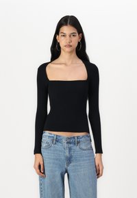 Black ribbed long-sleeve top with a square neckline, fitted design, and textured fabric. Paired with light blue straight-leg jeans.