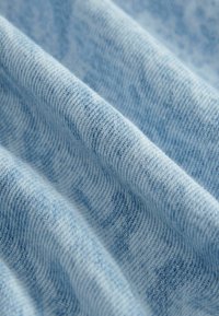Tessuto di cotone azzurro chiaro con una trama texturizzata, caratterizzato da dolci ondulazioni e sottili variazioni di colore, che creano un aspetto morbido e accogliente.