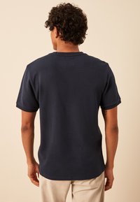 Marineblauw kortemouwenshirt van een gestructureerde stof, met een ronde zoom en een ribgebreide ronde hals, weergegeven vanaf de achterkant.