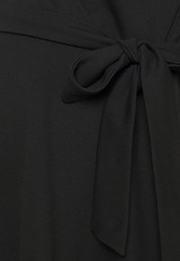Un tejido negro de textura suave presenta un detalle de cintura atada, creando un aspecto ajustado. El diseño es simple y elegante, enfatizando la versatilidad.
