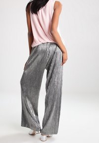 Pantalones de pierna ancha en un material plateado brillante con pliegues verticales; combinados con una blusa sin mangas de color rosa suave y zapatos de tacón bloque blanco.