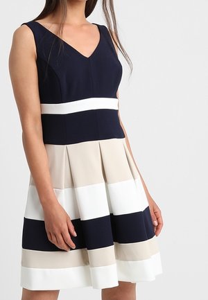 Ærmeløs V-hals kjole med tætsiddende navy krop, hvid taljebånd og plisseret nederdel med navy, beige og hvide vandrette striber.