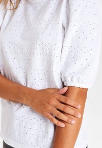 White textured blouse with puffed short sleeves and small cutouts. Features a relaxed fit and subtle striped pattern.