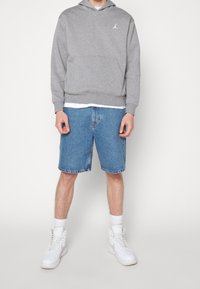 Gray hoodie with white logo, paired with blue denim shorts. White sneakers complete the outfit. Simple design and relaxed fit.