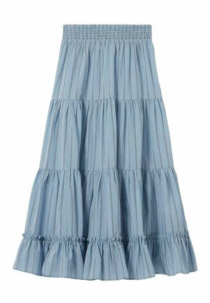 Donna con indosso un top rosa a fiori a maniche lunghe, gonna maxi azzurro chiaro a strati, sneakers blu navy, e che tiene una borsa nera con portachiavi.