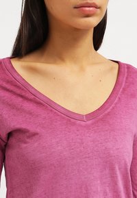 V-kaula-aukollinen, pitkähihaisen paita yksivärisessä magentan sävyssä, valmistettu pehmeästä, kevyestä kankaasta, jossa on hienovarainen tekstuuri.