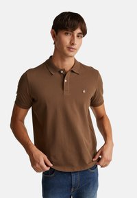 Hnědá bavlněná polo košile s klasickým límečkem, krátkými rukávy, výstřihem na tři knoflíky a malým vyšitým logem na hrudi.
