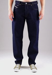 Dunkelblaue Jeans aus Denim mit geradem Schnitt, Fünf-Taschen-Design, kontrastierenden Nähten und Knopfverschluss. Kombiniert mit grünen Sneakern.