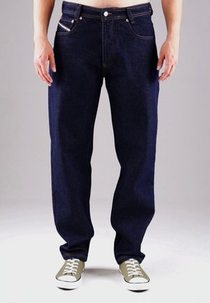 Dunkelblaue Jeans aus Denim mit geradem Schnitt, Fünf-Taschen-Design, kontrastierenden Nähten und Knopfverschluss. Kombiniert mit grünen Sneakern.