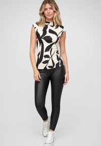 Top a coste nero e crema con motivo floreale, abbinato a leggings neri e sneakers bianche. Design aderente e stile senza maniche.