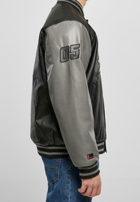 Herrarnas bomberjacka med en svart lä kropp, grå lä sleeves, ribbade manschetter och en broderad "05" på vänster ärm.
