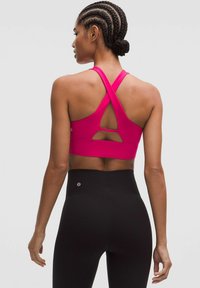Sujetador deportivo fucsia con tirantes cruzados y detalle recortado en la parte posterior, combinado con leggings negros de cintura alta. Tejido suave y elástico.