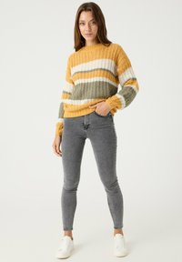 Sweater de punto con rayas amarillas, verdes y blancas, con un dobladillo y puños acanalados. Combinado con jeans ajustados grises y zapatillas blancas.
