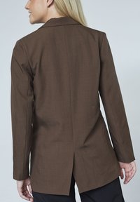 Brun skræddersyet blazer med en glat tekstur, enkelt split bagpå og lange ærmer. Vist fra en sidevinkel med moderne design.