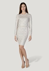 Pull en maille à motifs de couleur claire et jupe crayon ajustée, soulignés par un motif floral subtil. Le mannequin porte des escarpins couleur chair.