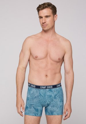 Blue boxer shorts featuring a leaf pattern, made of soft fabric. Black waistband with "CAMP DAVID" logo prominently displayed.