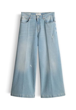 Jean large en denim bleu clair avec légère usure sur la cuisse gauche et le genou droit, poches avant, et fermeture par bouton.
