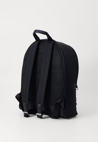 Sac à dos noir avec une forme arrondie, doté d'un panneau arrière en maille et de bretelles rembourrées et réglables. Tissu lisse avec des détails matériels minimaux.