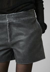 Sivkaste šорти iz žamša z gladko teksturo, stranskimi žepi in čistim oblikovanjem pasu. Tkanina se zdi mehka in prilagodljiva.
