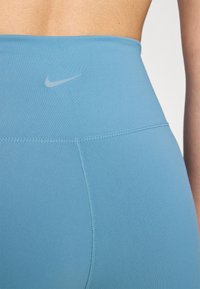 Leggings de culoare albastru deschis, cu talie înaltă, realizate dintr-un material neted, având un logo Nike subtil pe talie și cusături flatlock pentru confort.
