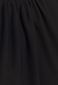 Tissu noir pour vêtement avec des fronces douces et un tissage subtilement texturé, montrant des plis et des drapés en gros plan.