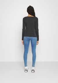 Langärmliges schwarzes Oberteil mit weitem Ausschnitt, kombiniert mit hellblauen Skinny-Jeans und weißen Sneakers mit schwarzen Akzenten.