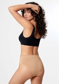 Schwarzer Sport-BH und hautfarbene, hochgeschnittene Unterwäsche. Glattes, elastisches Material mit minimalen Nähten. Das Modell dreht sich um und hebt die Passform und das Design hervor.