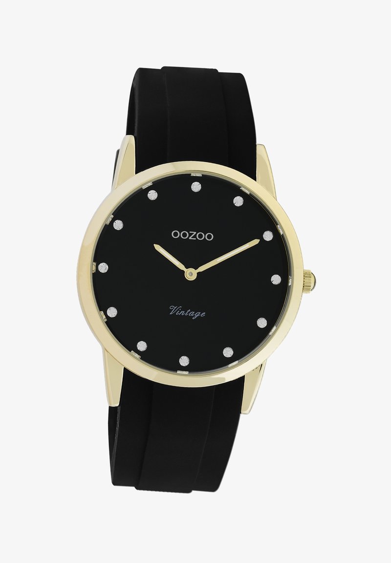 Montre noire avec un boîtier rond en or, marqueurs d'heure en cristal et aiguilles dorées. Dispose d'un bracelet en silicone noir. Le texte indique "Vintage".