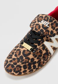 Leopard print sneaker featuring a black lacing system, a quilted upper, white side accents, and a gold logo plate on the tongue.