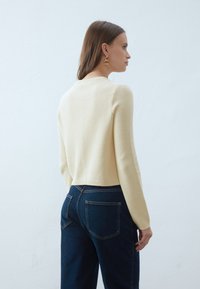Kremowy sweter z dzianiny o teksturowanym wykończeniu, okrągłym dekolcie i długich rękawach, w połączeniu z jeansami w kolorze ciemnoniebieskim o wysokim stanie.